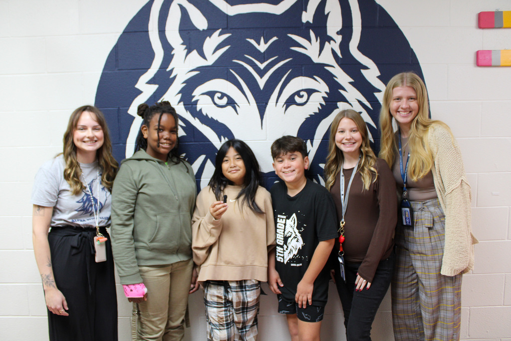 three teachers and three students stand in front of Wesmere Wolf logo on wall