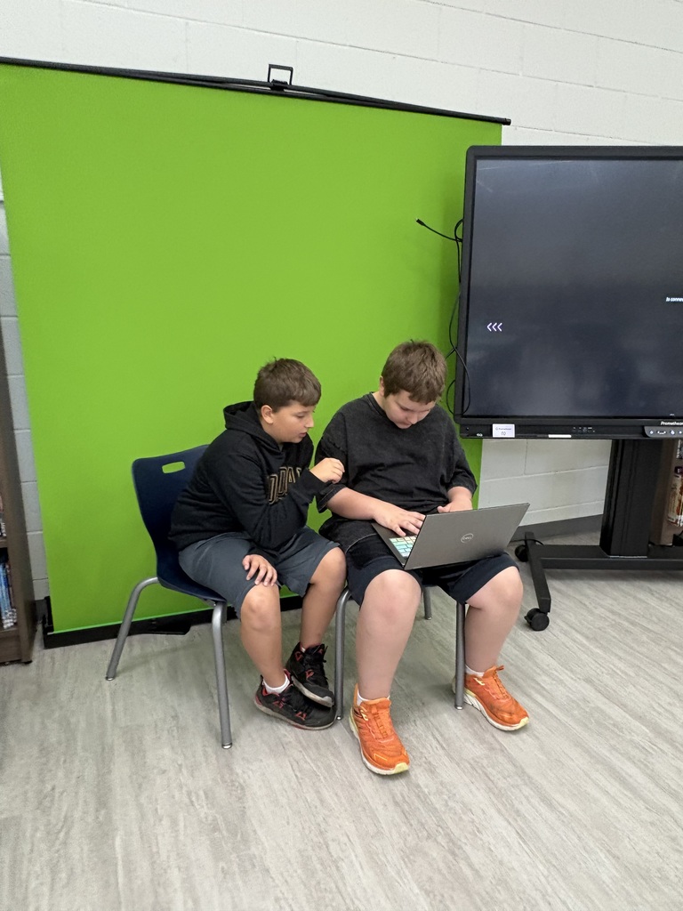 Two students working on a computer in front of a green screen