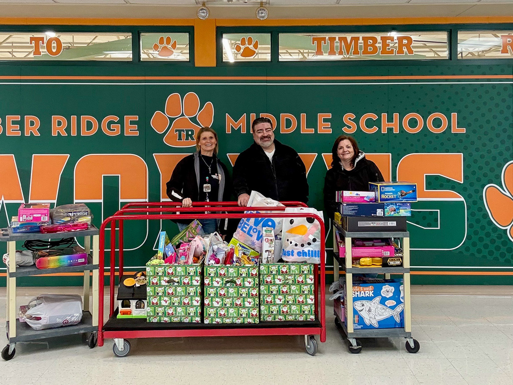 three people stand in front of group of donated toys