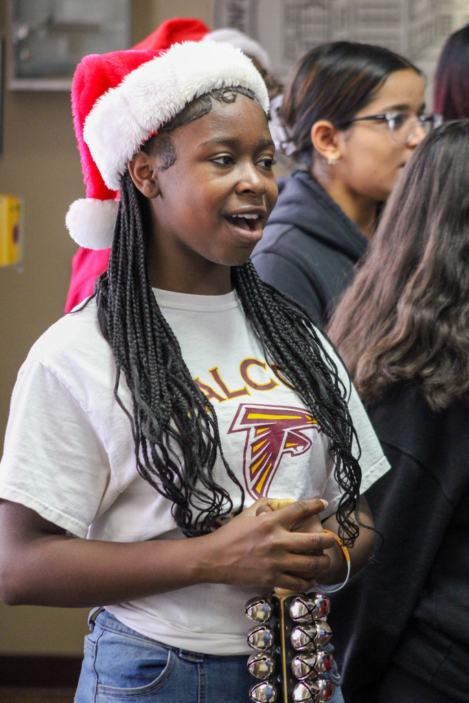 middle school girl wearing Santa hat sings and plays sleigh bells