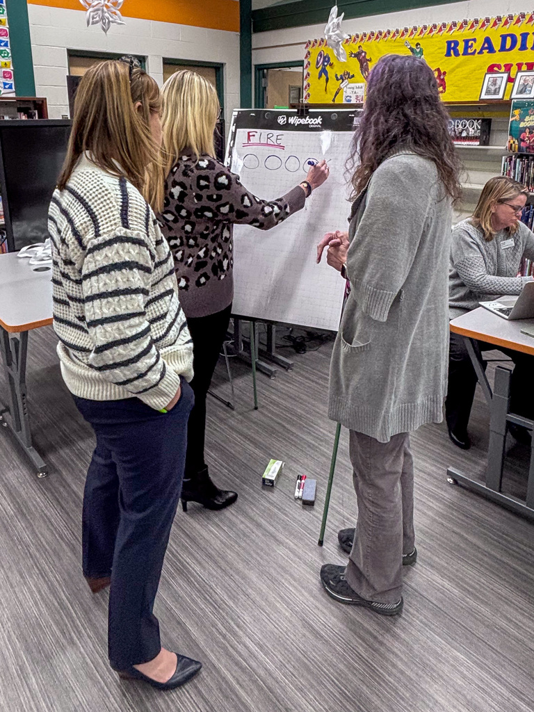 three people write on big pads of paper on an easel for an exercise during professional development