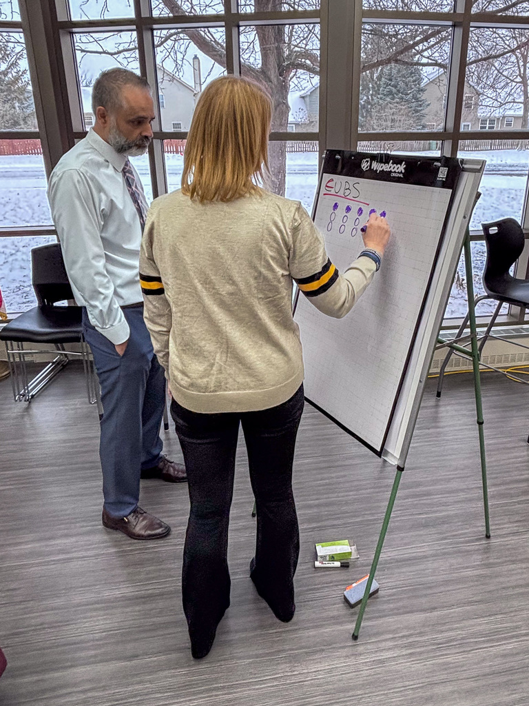 Two people stand near easels and write on big pads of paper for an exercise during professional development