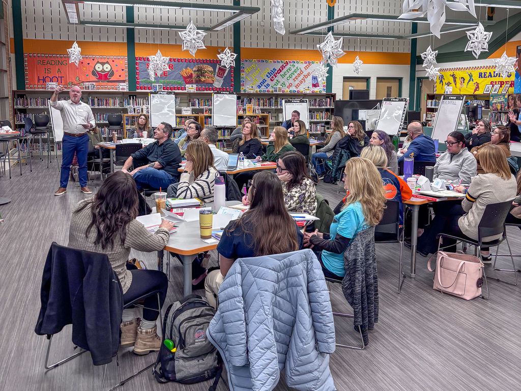 a group of people sit at tables and listen to a speaker for an exercise during professional development