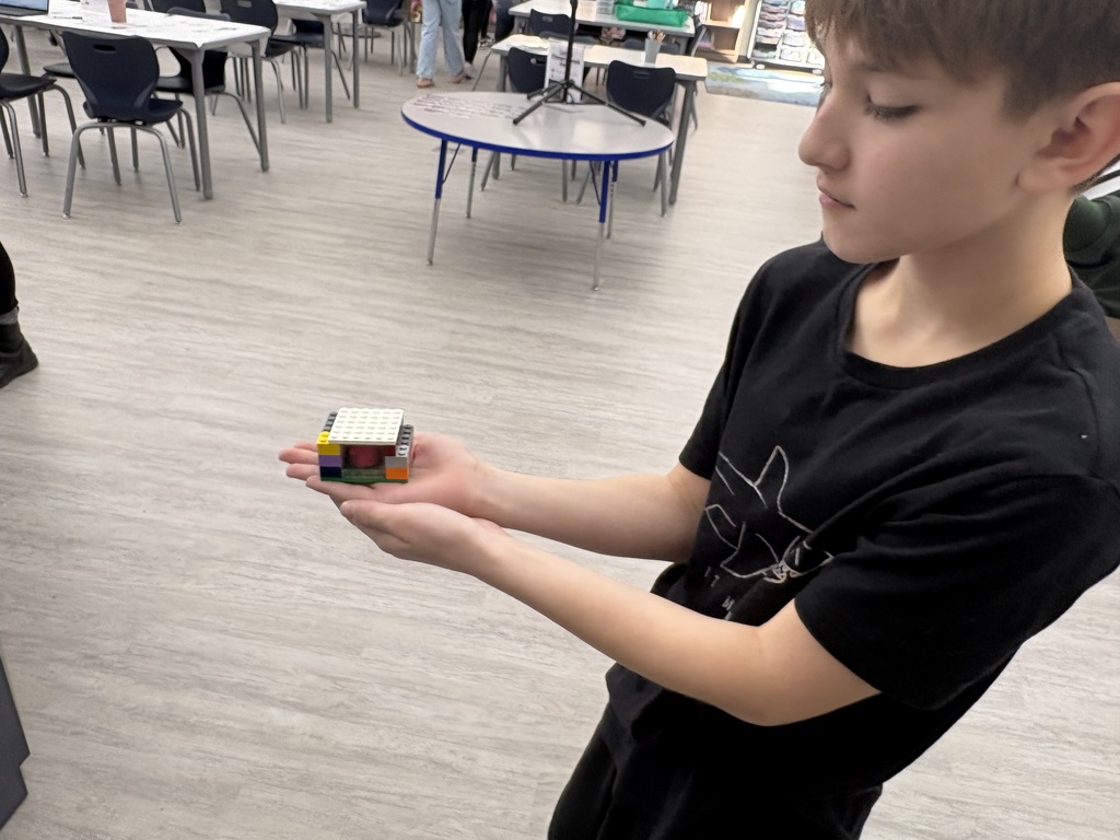 A student is showing a small structure he built in the library. 