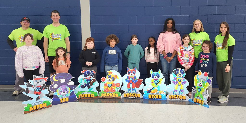 Students and teachers standing in front of cardboard, cut outs in a school gym