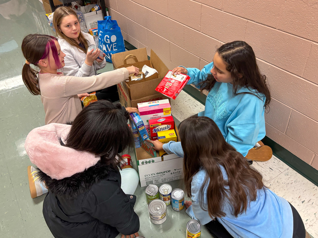 group of students sit on floor and pack food into boxes