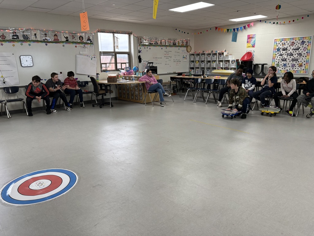 Students watch a scooter slide on top of a circle on the floor. 