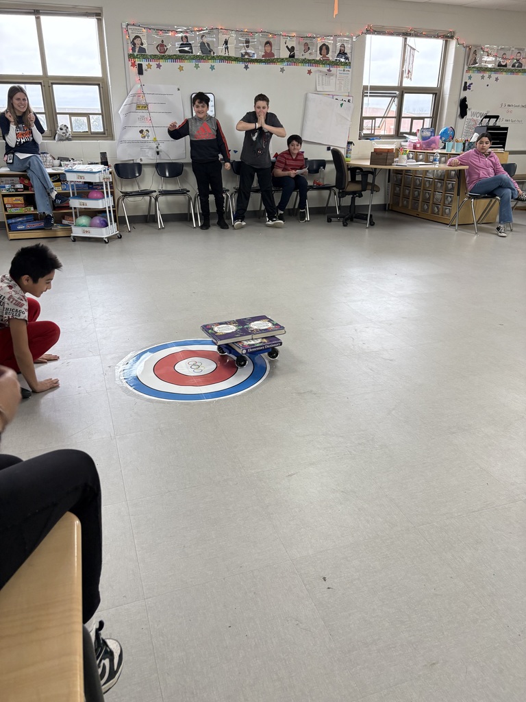 Students watch a scooter slide on top of a circle on the floor. 