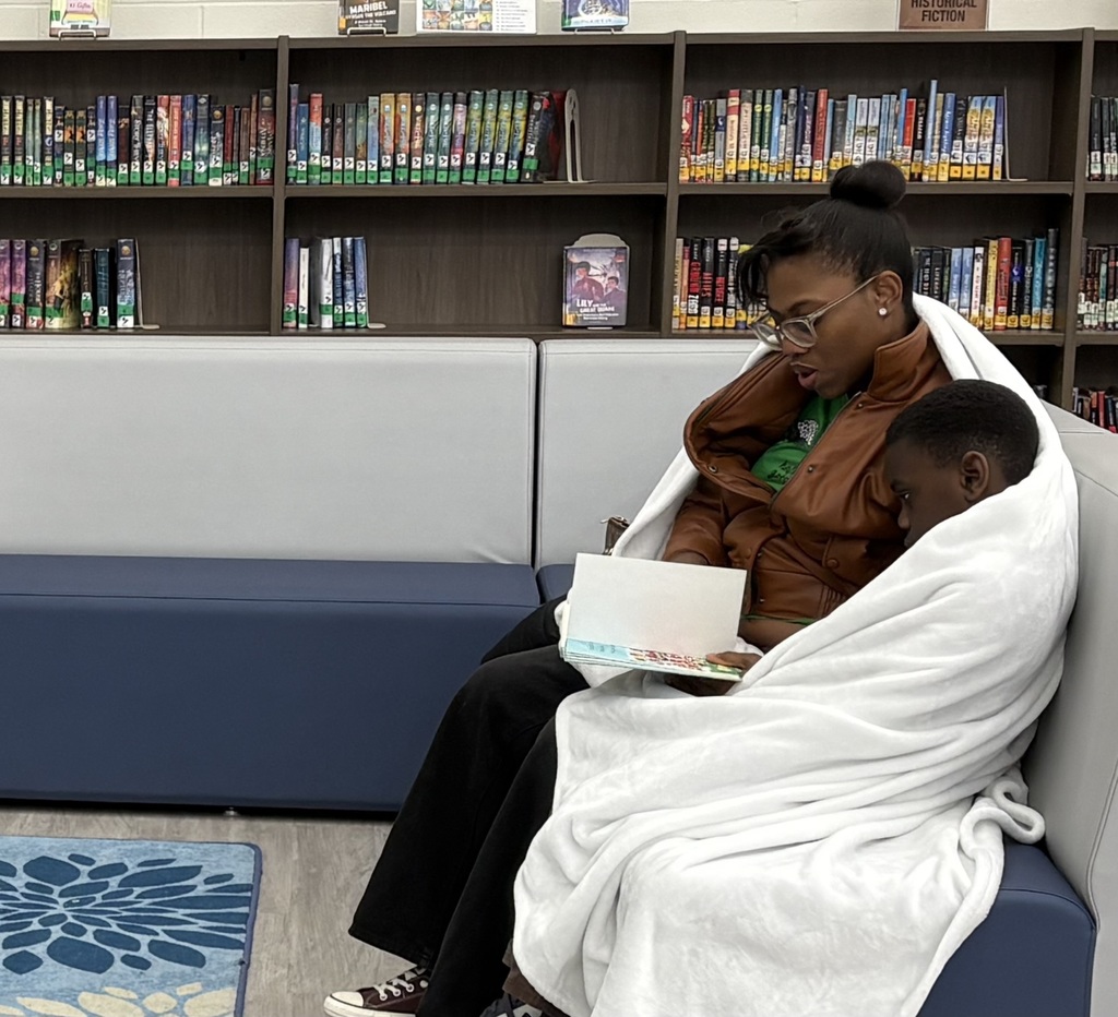 A mom and son sitting in a library on a couch reading