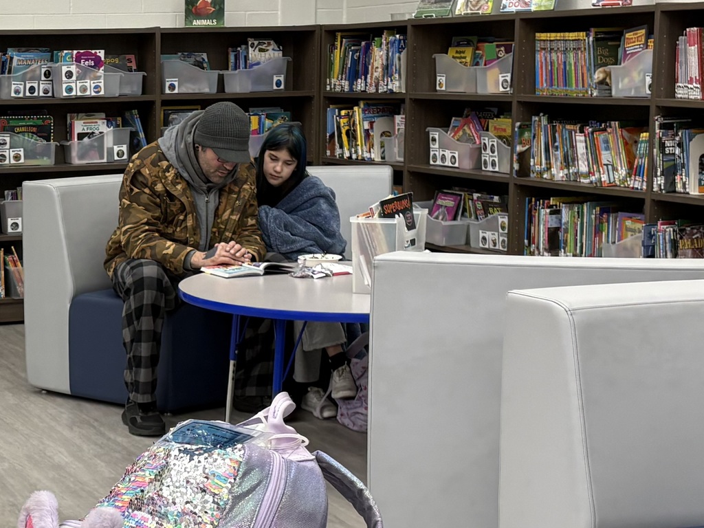 A father and daughter sitting on a couch in a library reading. 