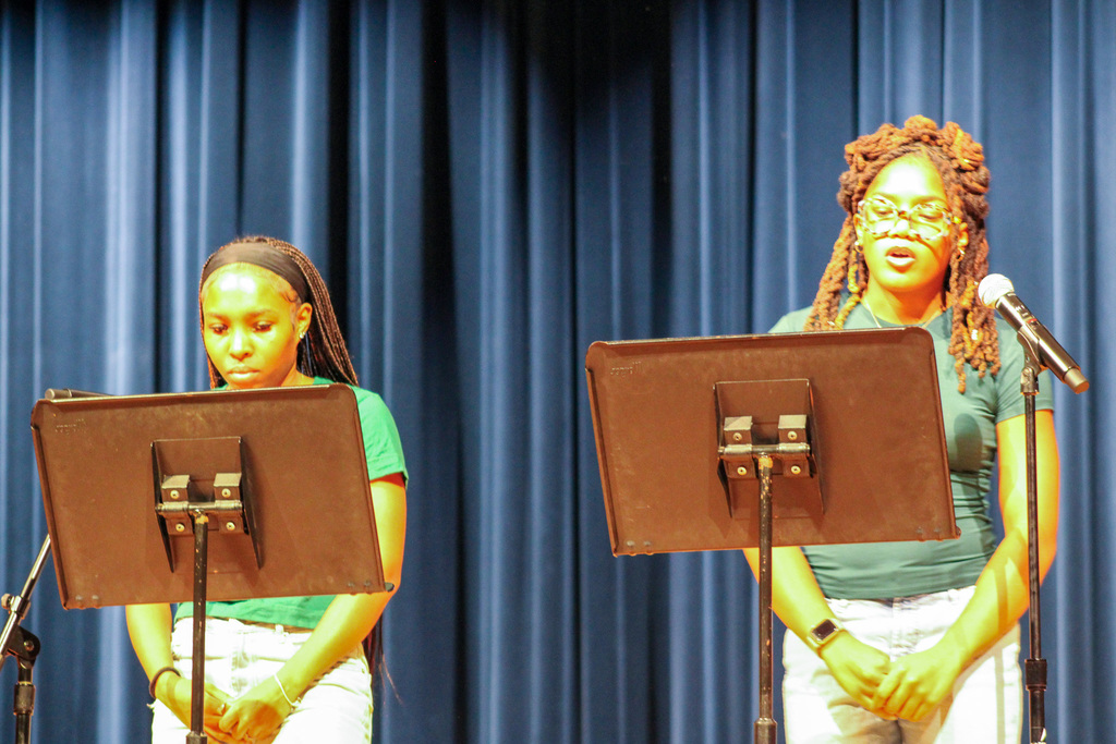 two female students stand in front of two music stands on stage