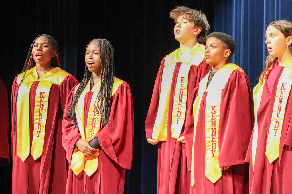 Five John F.  Kennedy Middle School students in choir robes sing on stage