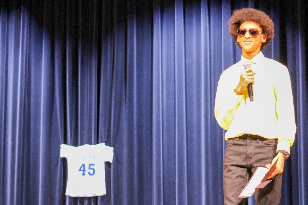 Student wearing sunglasses holding microphone on stage