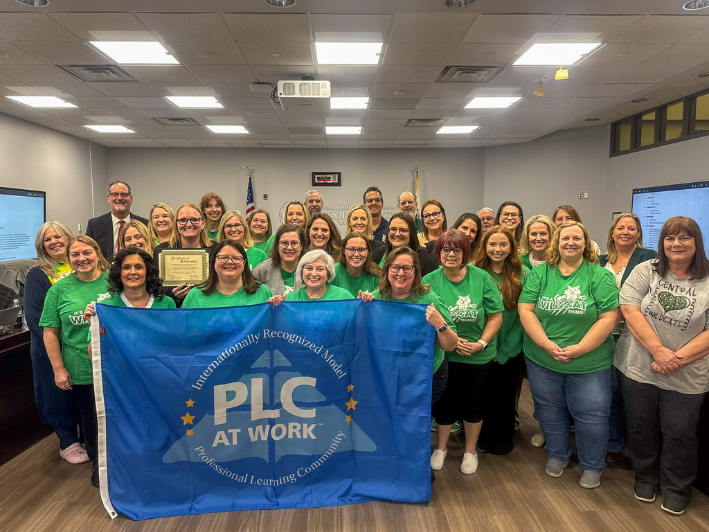 group of men and woman standing in board room holding blue flag PLC At Work