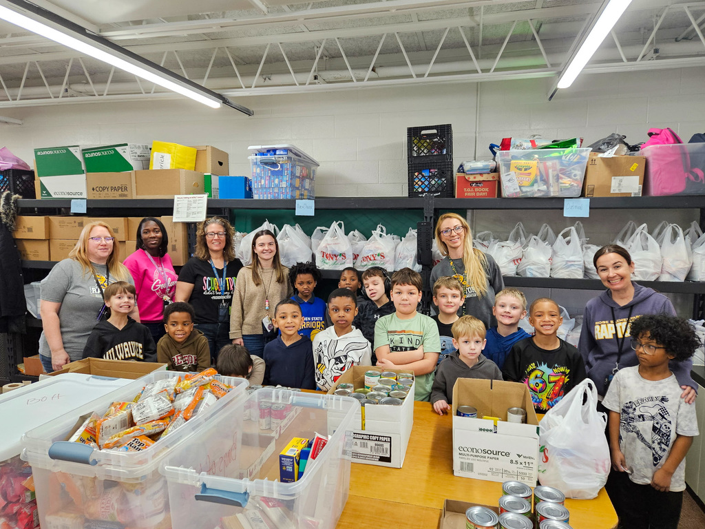 group of elementary school students and teachers stand in a classroom filled with food