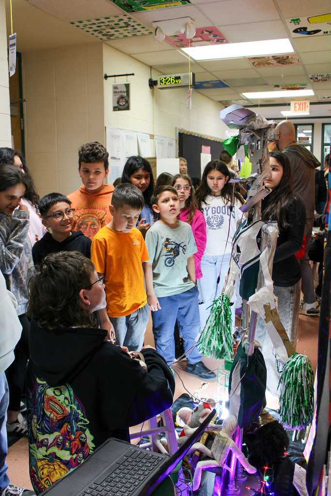 group of students watch a student run a homemade animatronic