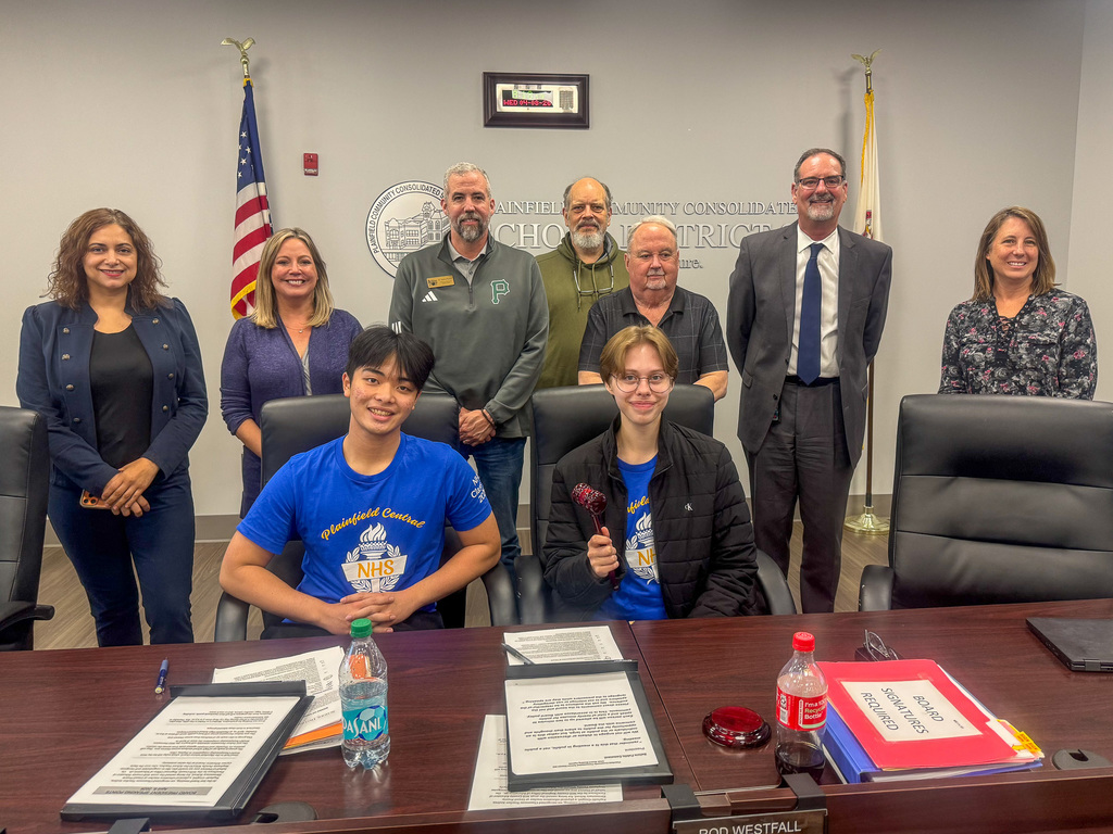 group of adults standing behind two students seated at table