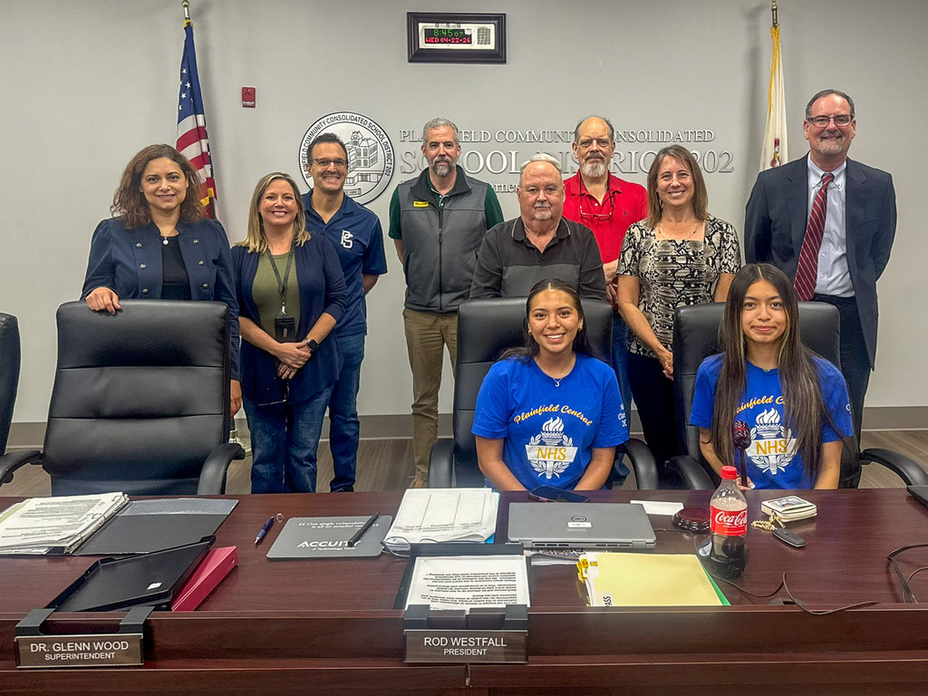 group of adults standing behind two students seated at table