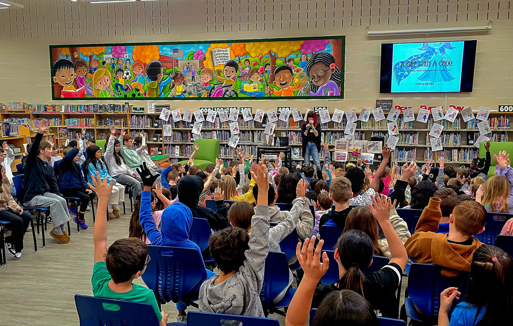 group of children sit listening to author while raising hands
