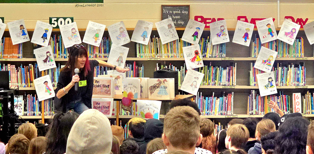 Woman with red streak in hair gestures to books set up on a stand