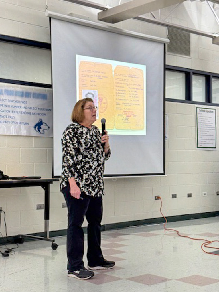 woman standing in front of students with microphone in front of projector screen