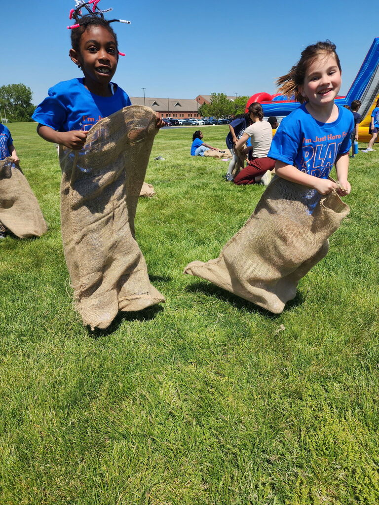 Two students jumping in burlap bags outside.