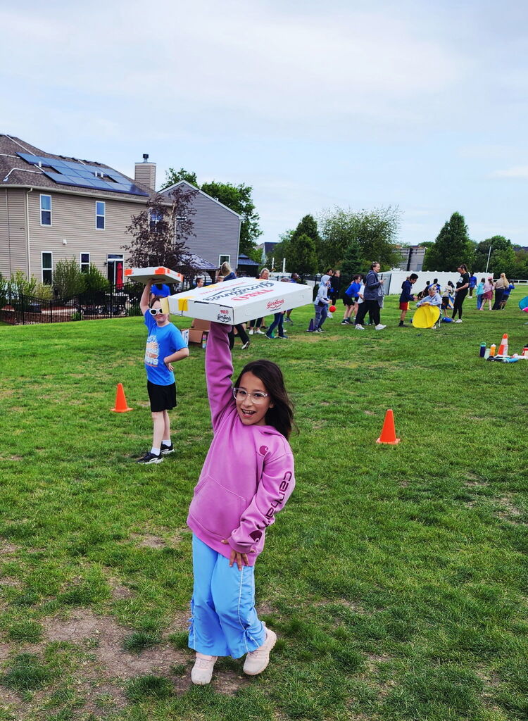 A student standing outside holding a pizza box. 