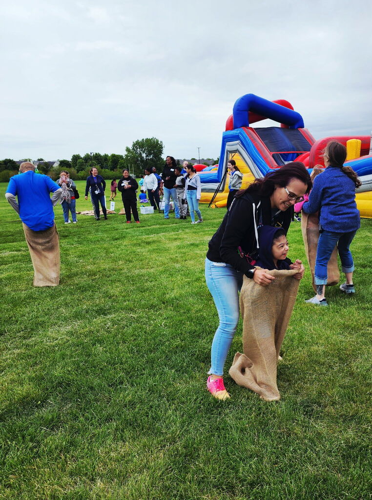 A teacher helps a student jump in a burlap bag. 