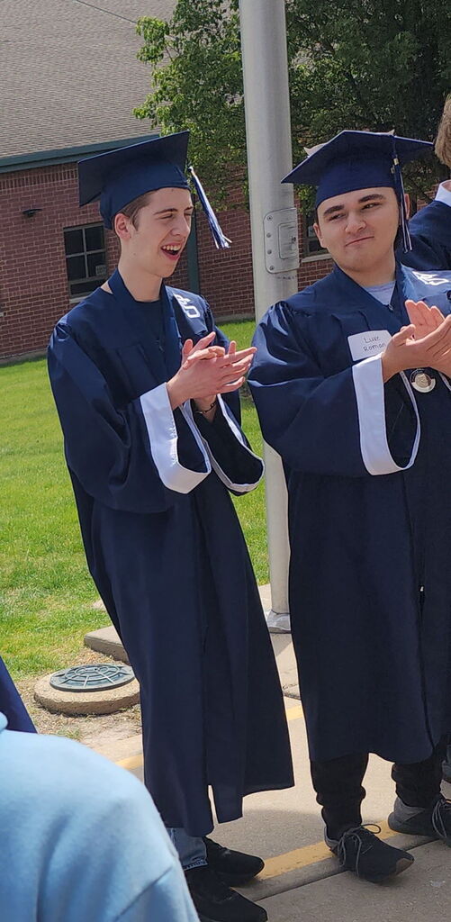 Two students in caps and gowns standing outside a school. 