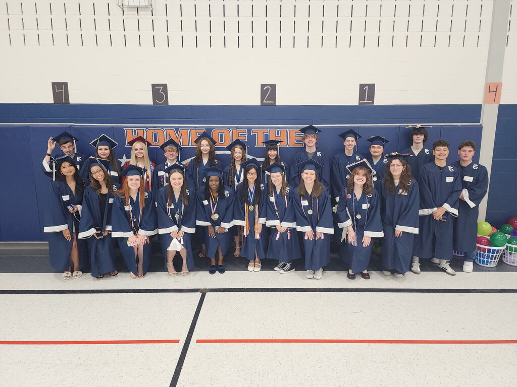Students in graduate caps and gowns posing in a gym.