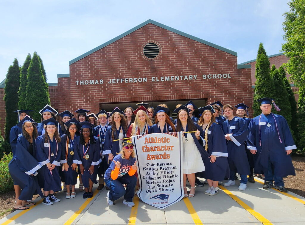 Students in graduate caps and gowns posing in front of a school 