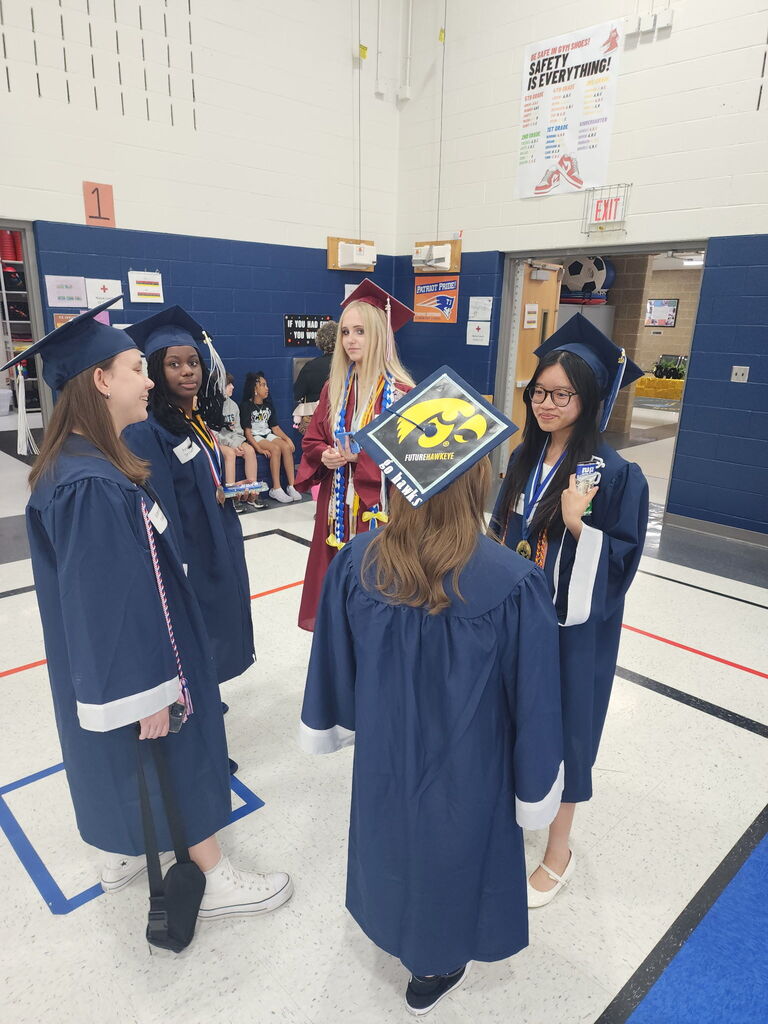 Students in caps and gowns standing in a gym. 