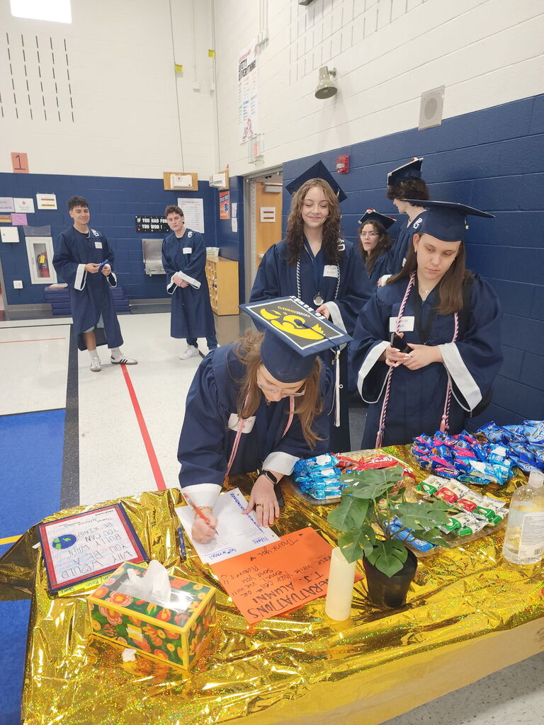 Students in caps and gowns signing in at a table.