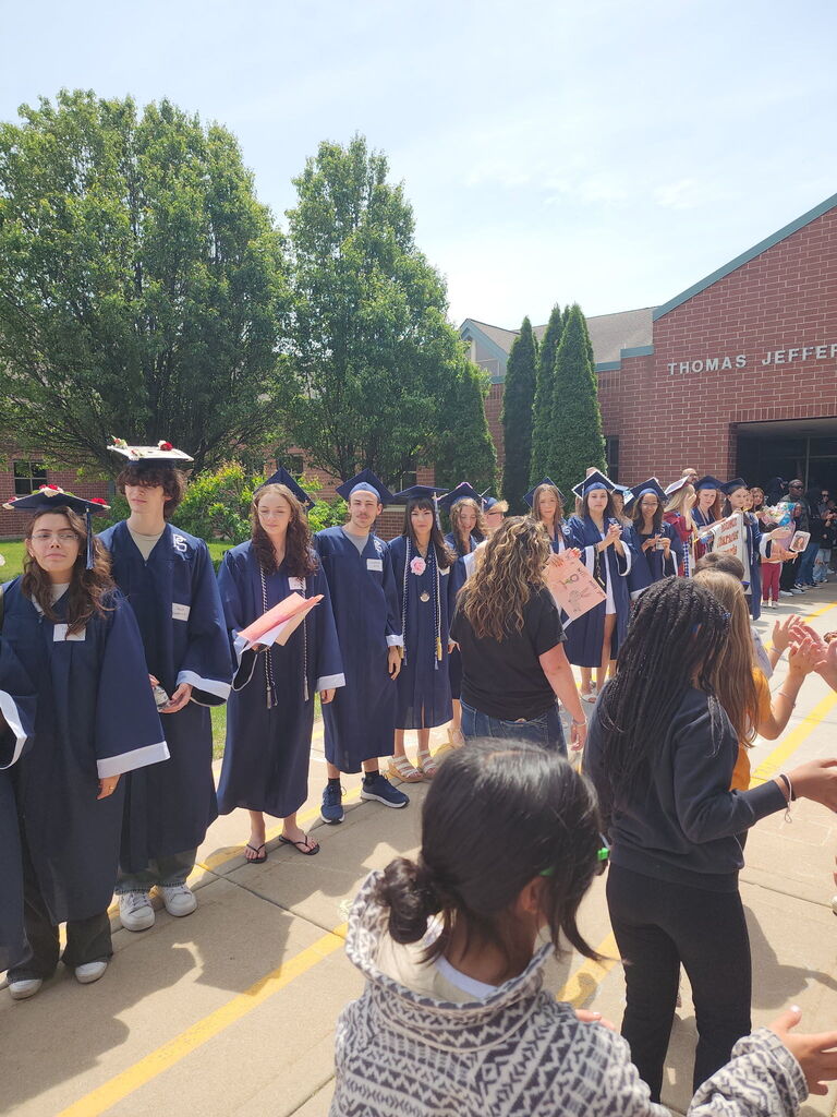 Students in caps and gowns standing outside a school.