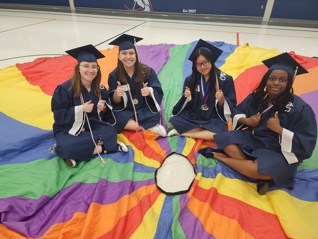 Students in a gym sitting on a colorful parachute. 