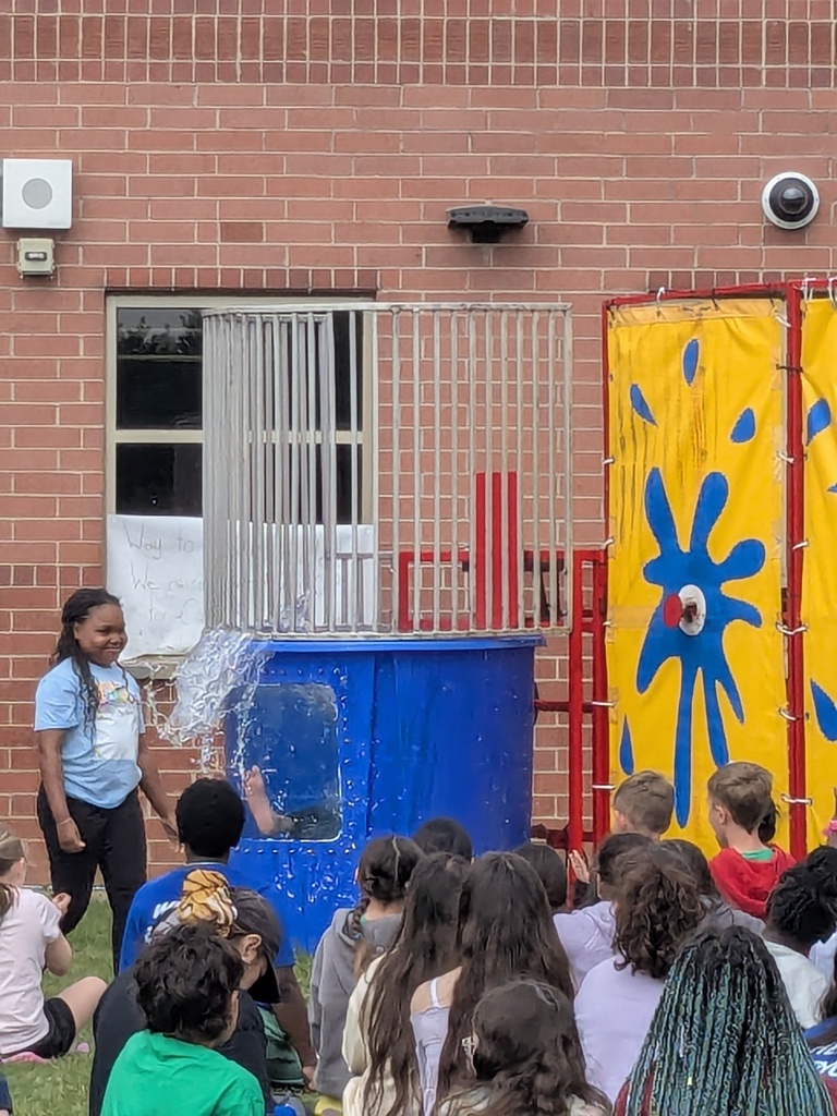 Principal Tyler Haymond takes a splash in a dunk tank outside with students watching. 