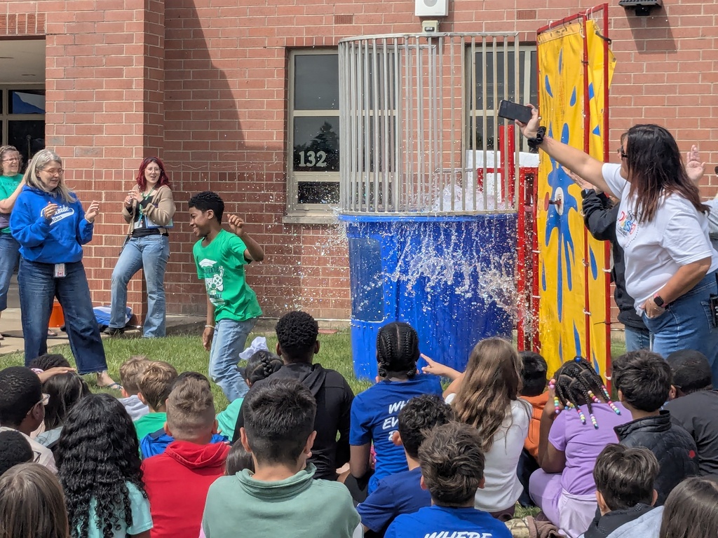 Principal Tyler Haymond takes a splash in a dunk tank outside with students watching. 