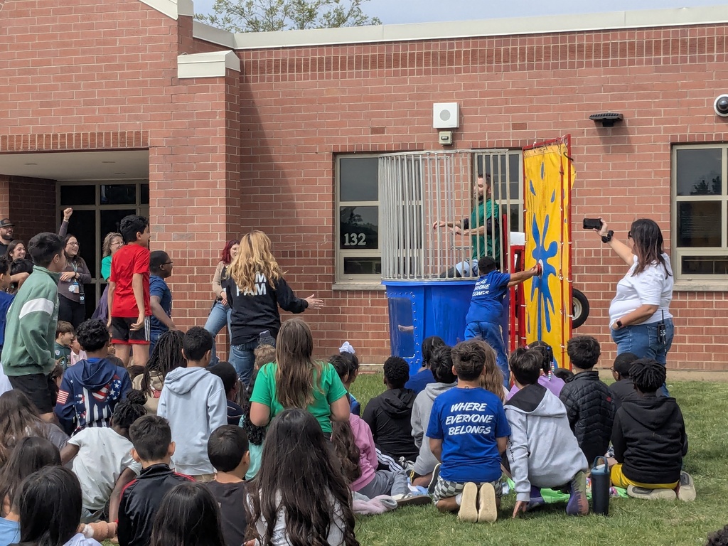 Principal Tyler Haymond takes a splash in a dunk tank outside with students watching. 