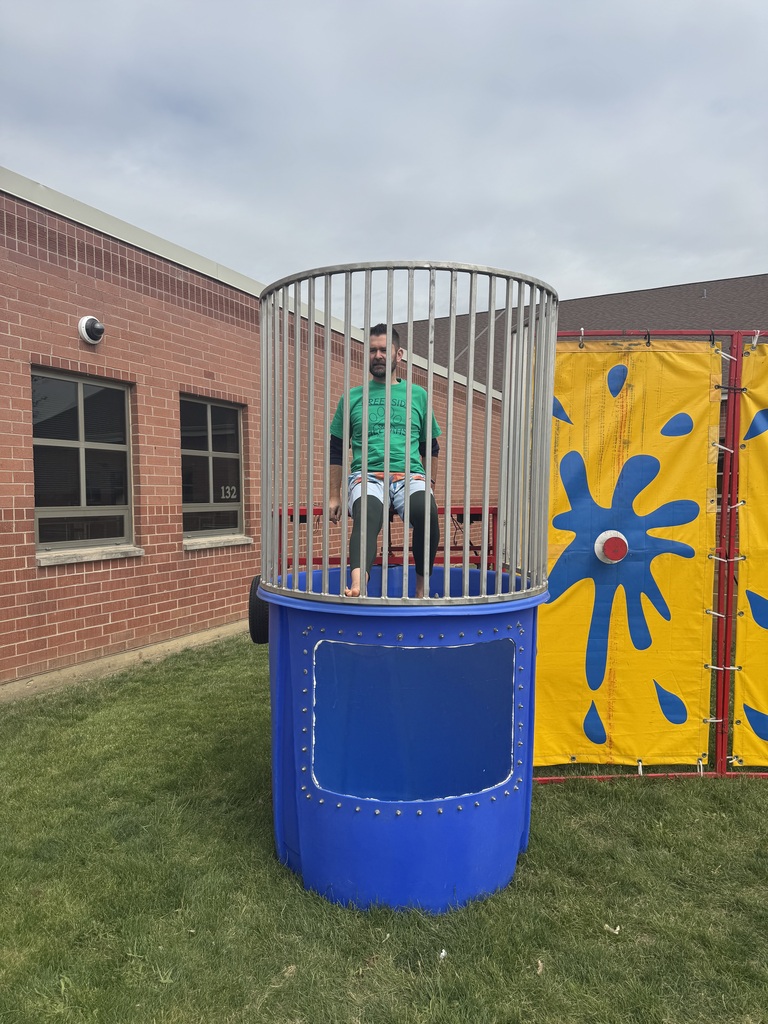 Principal Tyler Haymond takes a splash in a dunk tank outside with students watching. 
