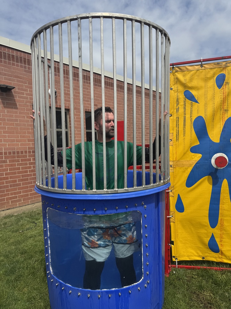 Principal Tyler Haymond takes a splash in a dunk tank outside with students watching. 
