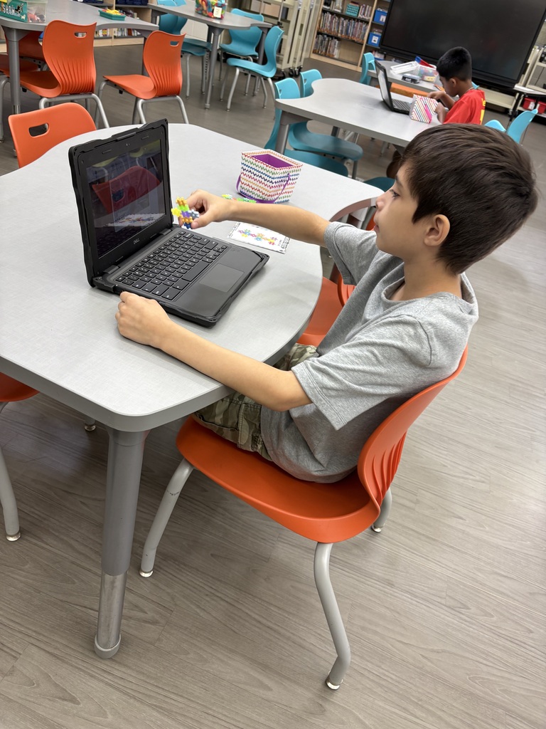 male student holds colorful building creation in front of laptop