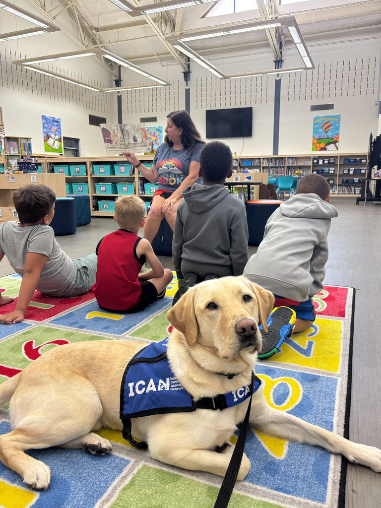 Facility dog Tater Tot lays on rug in front of students during story time