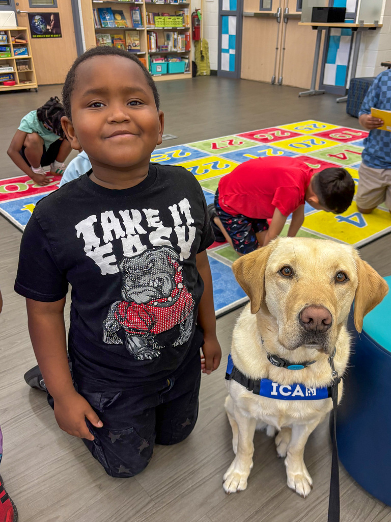 male elementary school students kneels next to Facility Dog Tater Tot