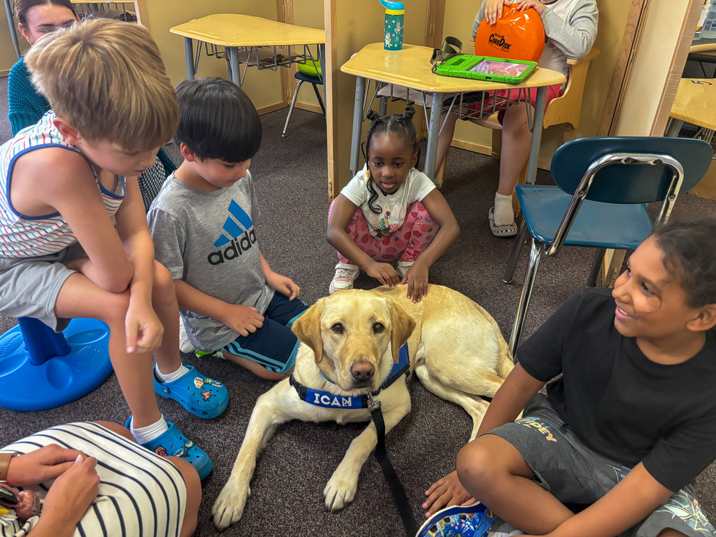 Facility Dog Tater Tot lays in the middle of a group of seated students