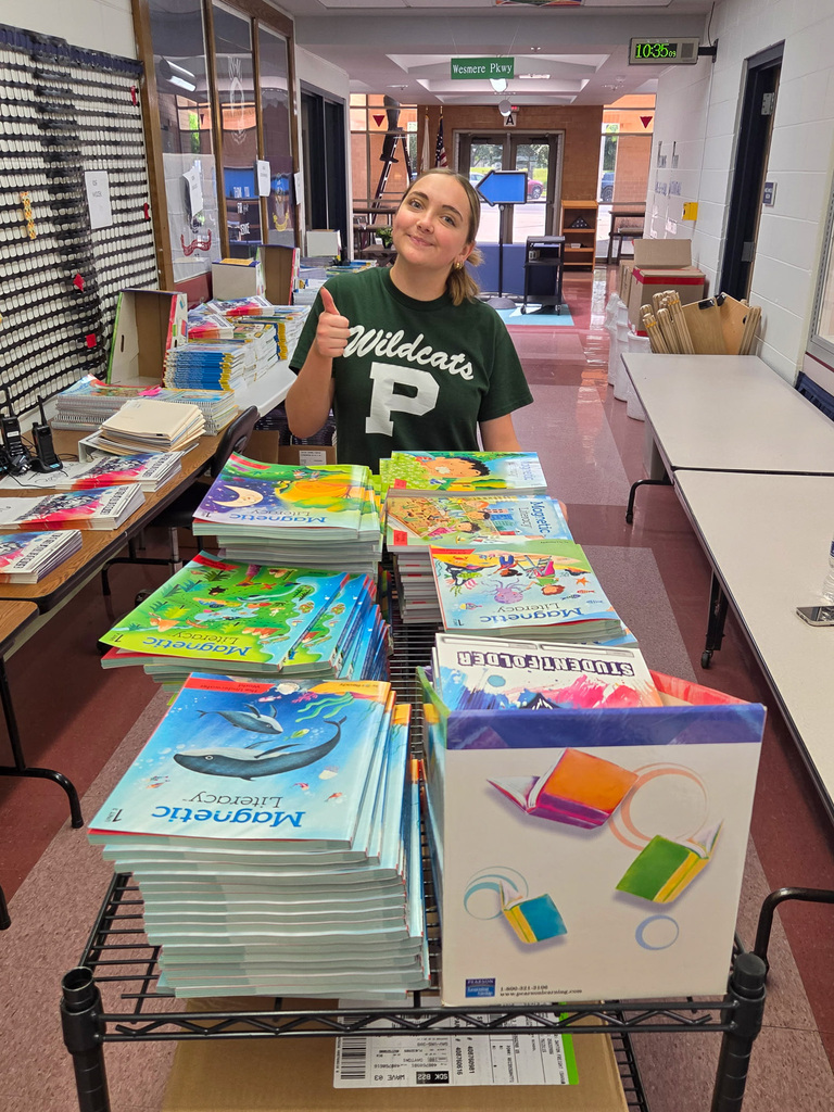 one high school girls doing a thumbs up behind a cart of books