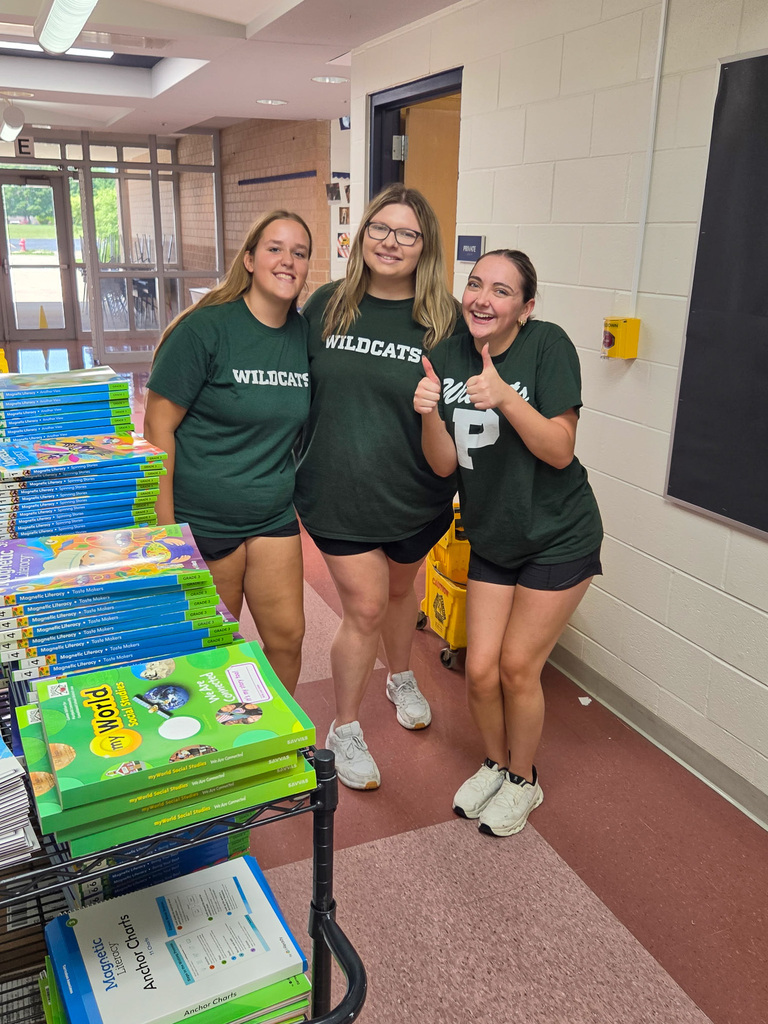 three high school girls stand in school hallway next to carts of books
