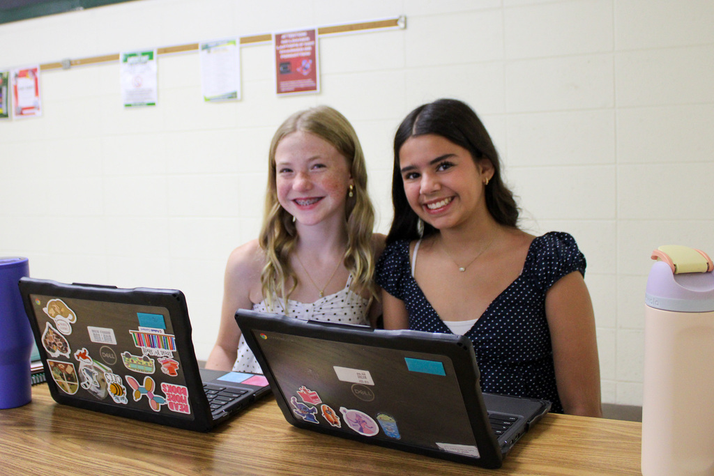 two students sit at table with laptops open on table