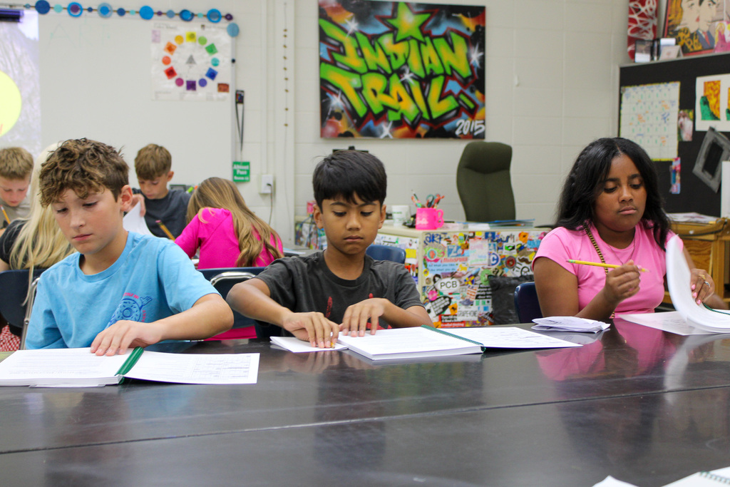 three students sit at table writing on agenda books