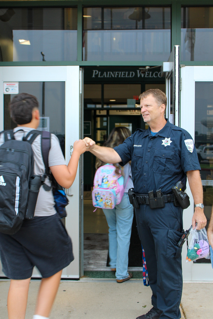 police officer give fist bump to student walking into school