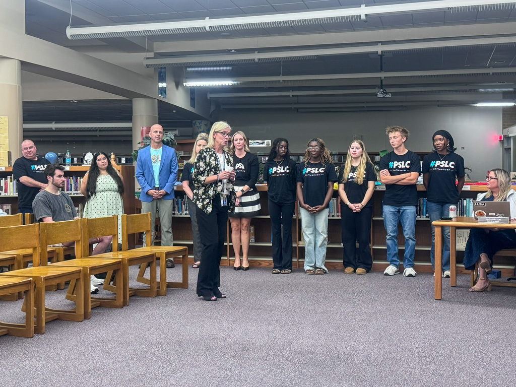 woman stands in front of group of students, teachers talking